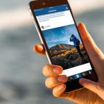 Gran Canaria, Spain - December 13, 2015: Woman watching Instagram news from RossHelen account with new iPhone 6s Space Gray on the blurred sea background. iPhone 6 was created and developed by the Apple inc. Instagram is a popular online social networking service. RossHelen is famous travel stock photographers